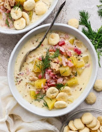 overhead photo of clam chowder with pork belly in a white bowl, plus oyster crackers