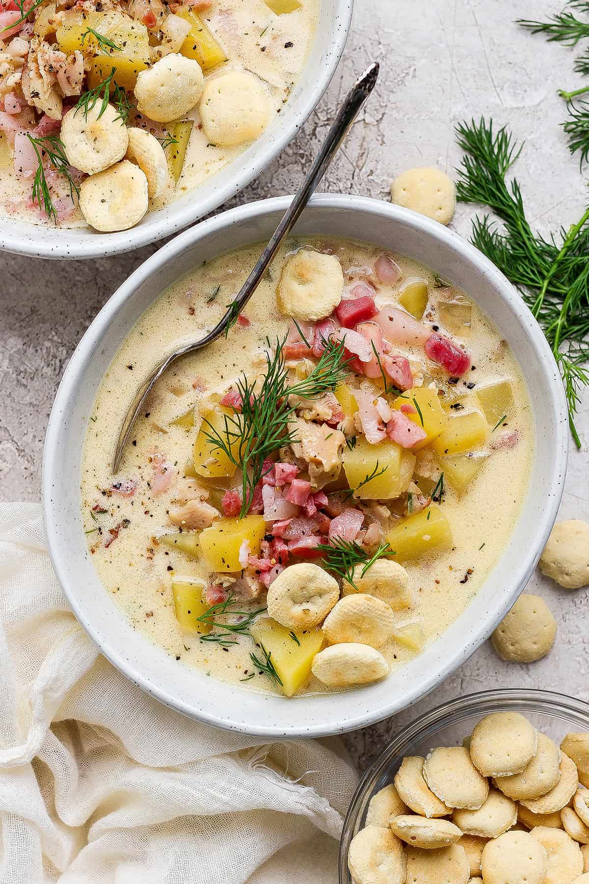 overhead photo of clam chowder with pork belly in a white bowl, plus oyster crackers