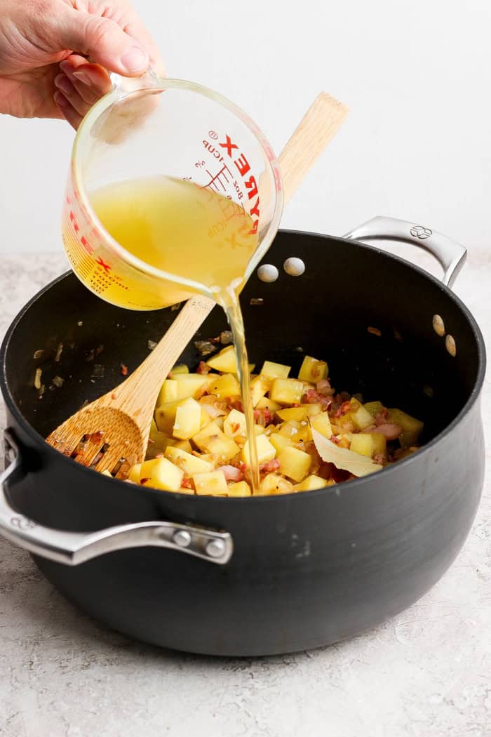 pouring chicken broth into a large black pot