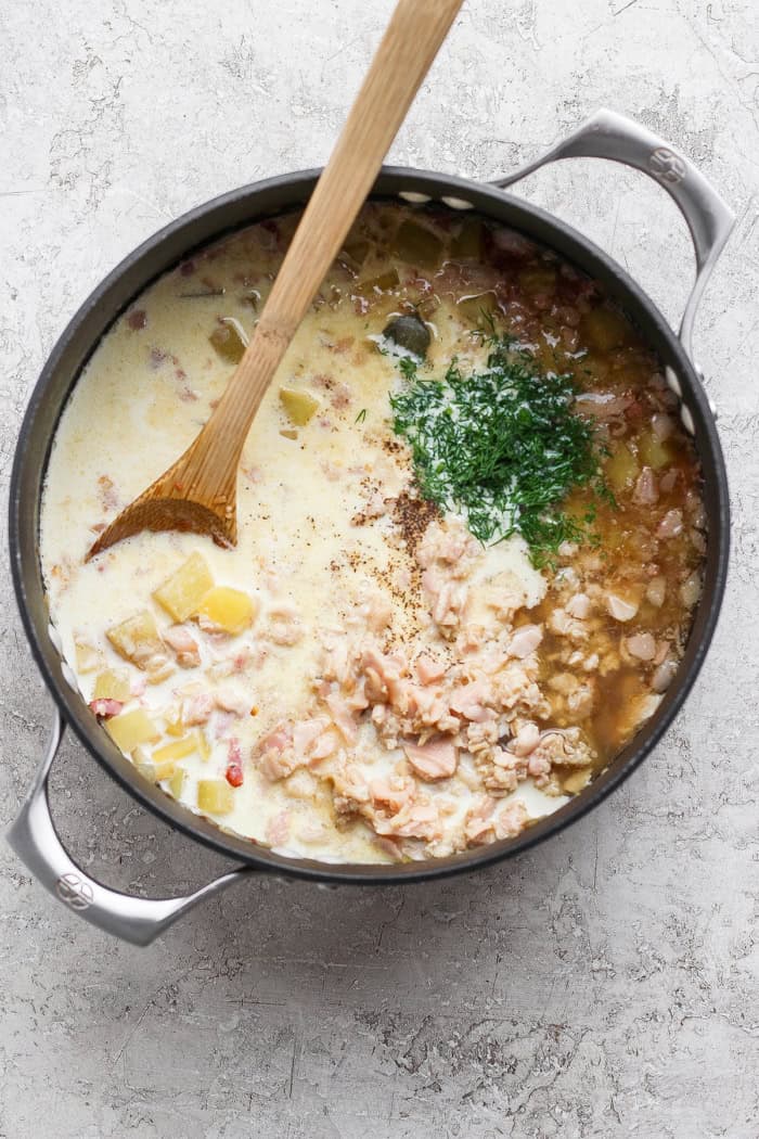 a wooden spoon in a large pot, combining ingredients for clam chowder