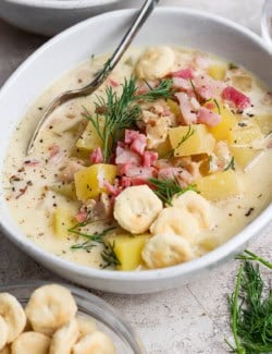 a white bowl of clam chowder with pork belly and oyster crackers