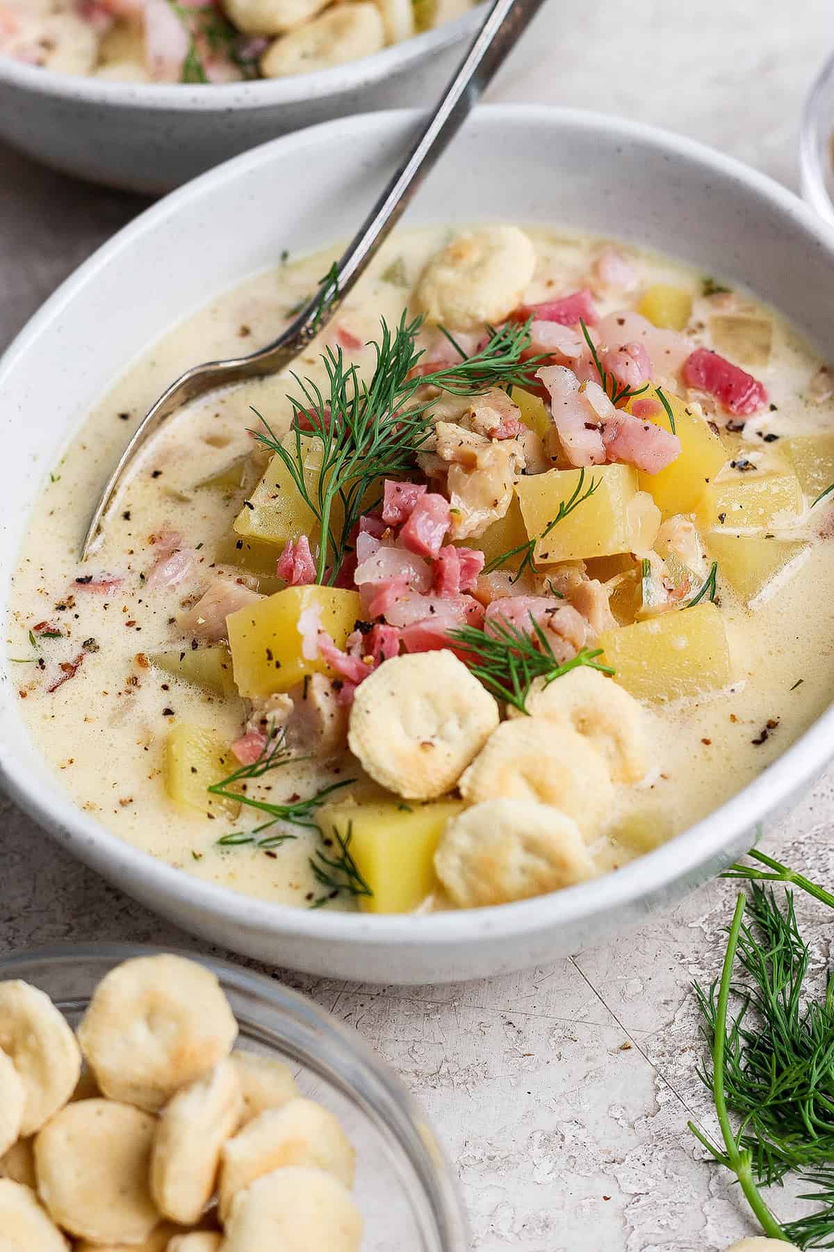 a white bowl of clam chowder with pork belly and oyster crackers