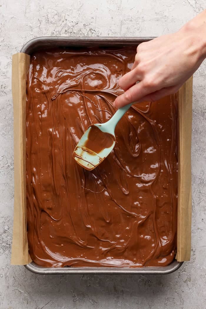 These scotcheroos are chewy, chocolatey, and peanut buttery, with a little sea salt to take them up a notch. An easy no-bake dessert recipe! Spreading chocolate layer onto pan of scotcheroos.
