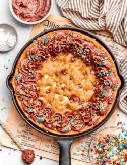 overhead photo of chocolate chip skillet cookie decorated with chocolate frosting and colorful sprinkles