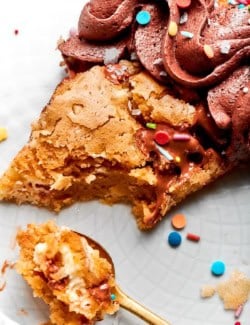 close-up photo of a piece of chocolate chip skillet cookie decorated with chocolate frosting and colorful sprinkles, with a spoonful removed