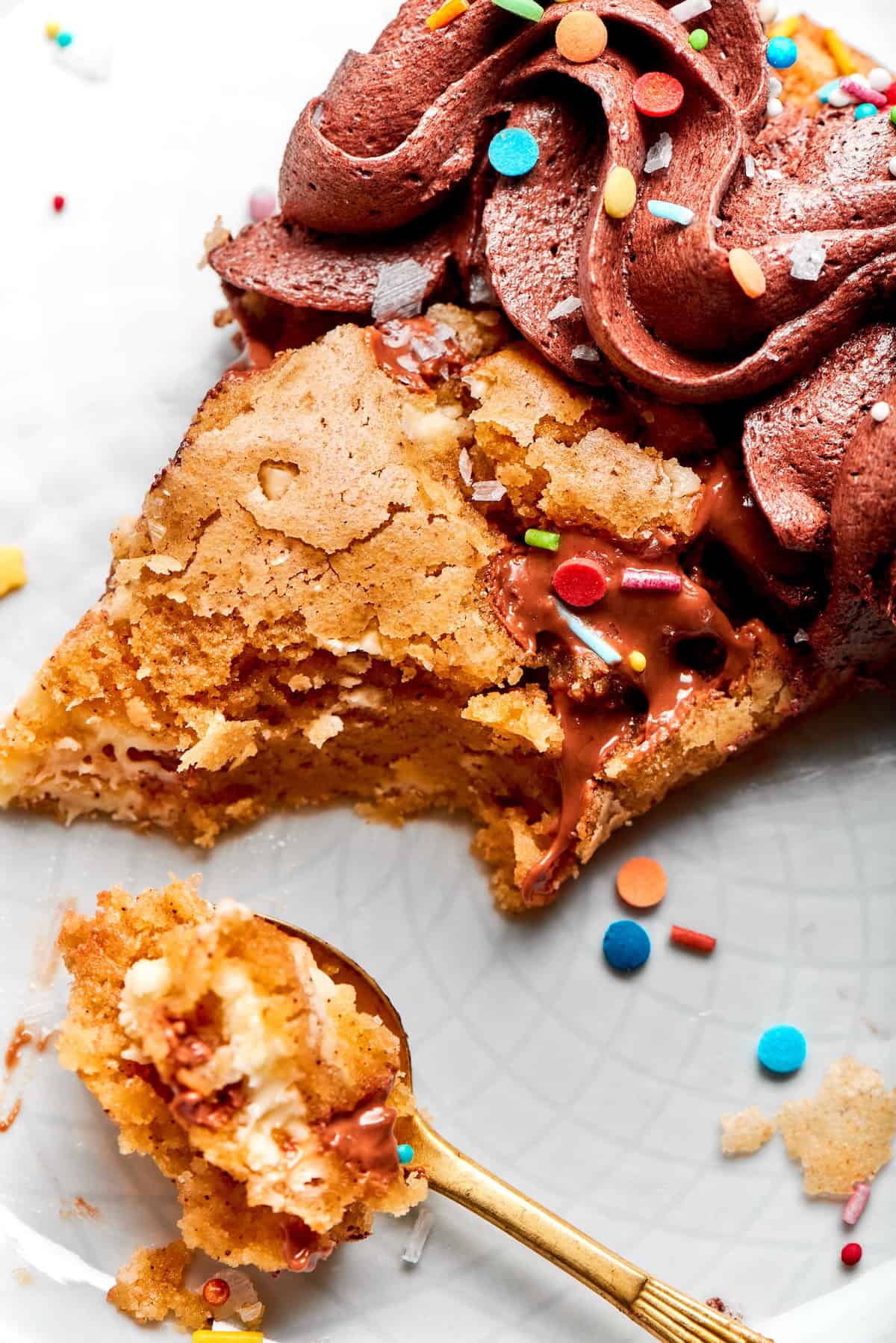 close-up photo of a piece of chocolate chip skillet cookie decorated with chocolate frosting and colorful sprinkles, with a spoonful removed