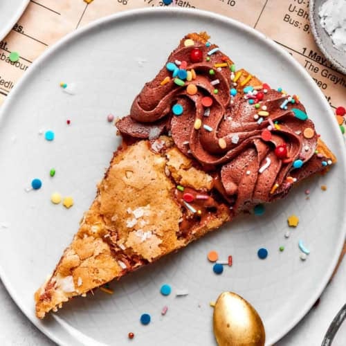 close-up photo of a piece of chocolate chip skillet cookie decorated with chocolate frosting and colorful sprinkles