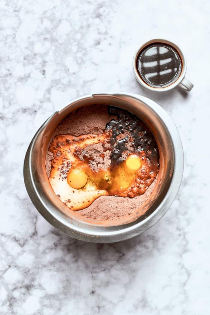 wet ingredients added to chocolate cake ingredients in a stainless steel mixing bowl
