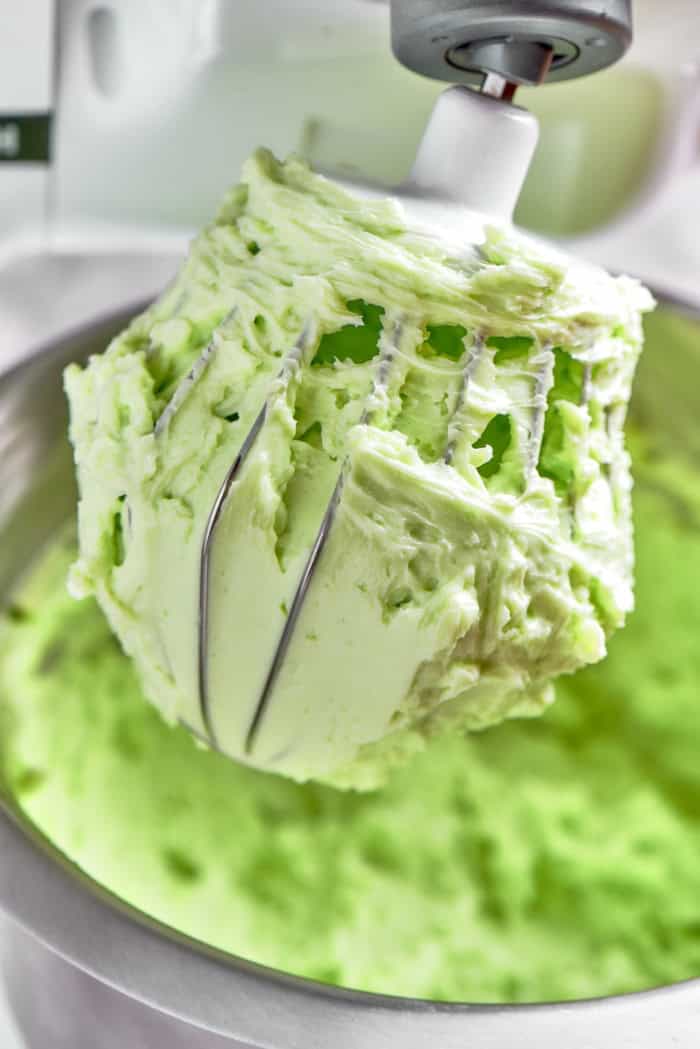 an electric stand mixer with mint buttercream in the bowl and on the whisk attachment