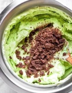 mixing mint buttercream with chopped chocolate, in a stainless steel bowl