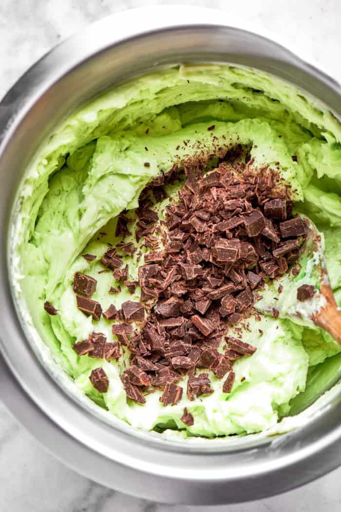 mixing mint buttercream with chopped chocolate, in a stainless steel bowl