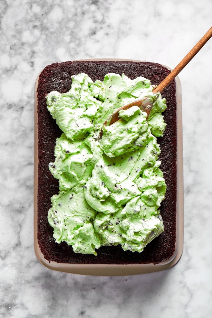 spreading mint chocolate chip buttercream over chocolate cake