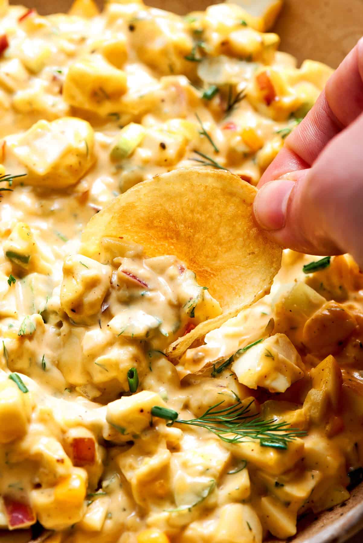 a hand dipping a potato chip into a bowl of egg salad