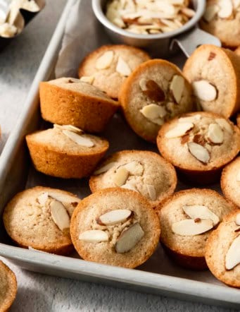 Financiers on sheet pan with bowl of almonds.