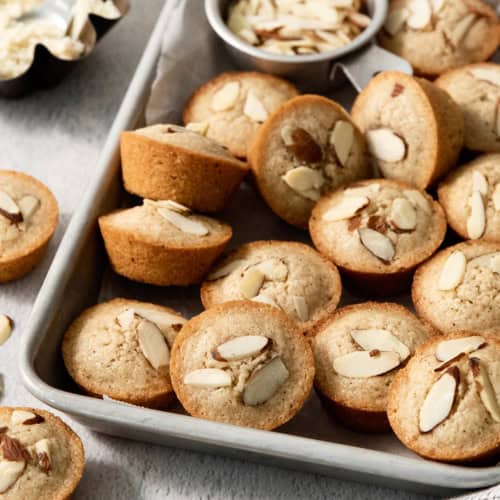 Financiers on sheet pan with bowl of almonds.