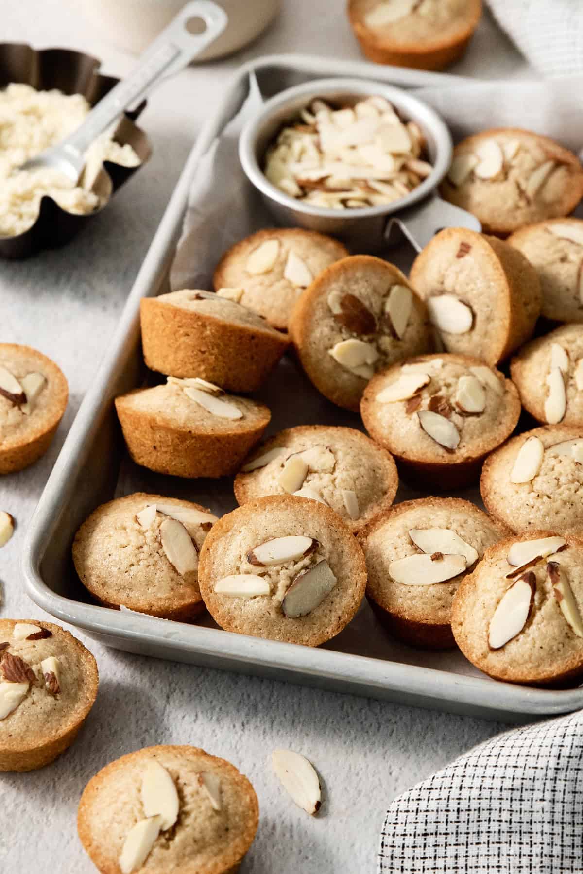 Financiers on sheet pan with bowl of almonds.