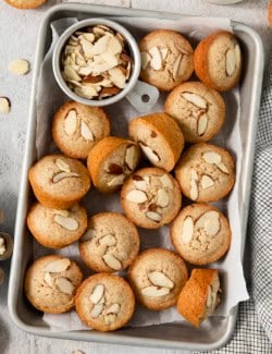 Sheet pan with financiers and cup of sliced almonds.