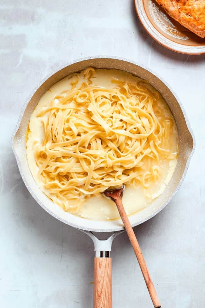 Stirring fettuccine into skillet of alfredo sauce.