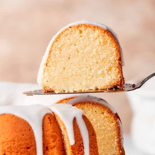 a piece of glazed cream cheese pound cake being lifted away from the whole cake