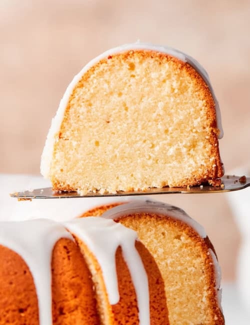 a piece of glazed cream cheese pound cake being lifted away from the whole cake