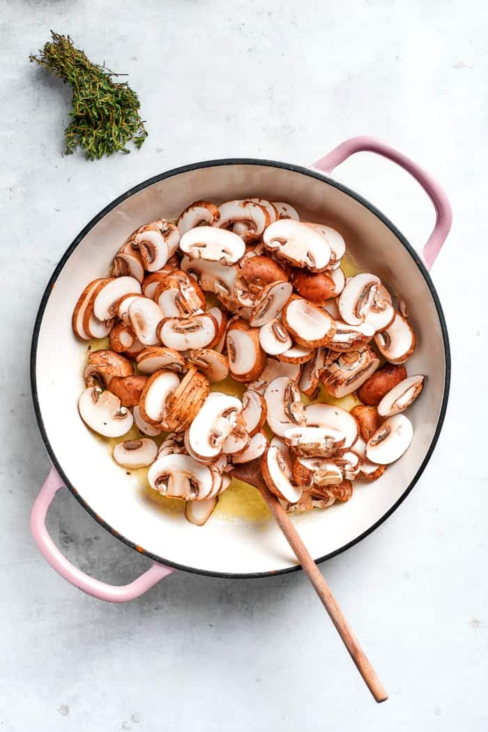 Mushrooms and butter in skillet with wooden spoon.