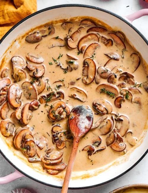 creamy mushroom sauce in a round pink braiser, with a wooden spoon