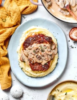 Plate of mashed potatoes and steak with creamy mushroom sauce.