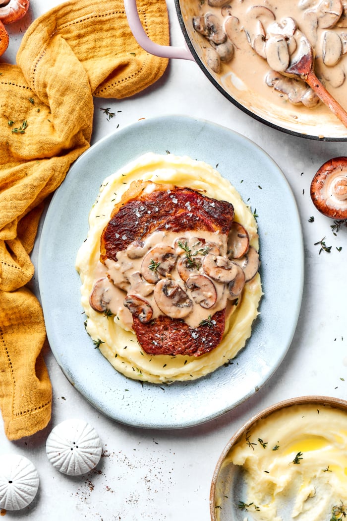 Plate of mashed potatoes and steak with creamy mushroom sauce.
