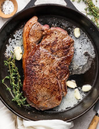 Steak in cast iron skillet with thyme, garlic cloves, and butter.