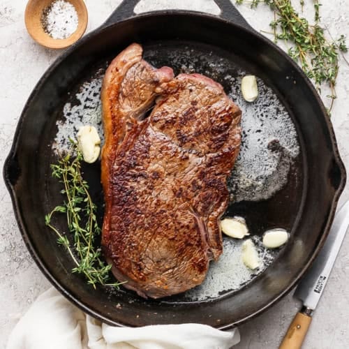 Steak in cast iron skillet with thyme, garlic cloves, and butter.