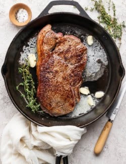 Steak in cast iron skillet with thyme, garlic cloves, and butter.