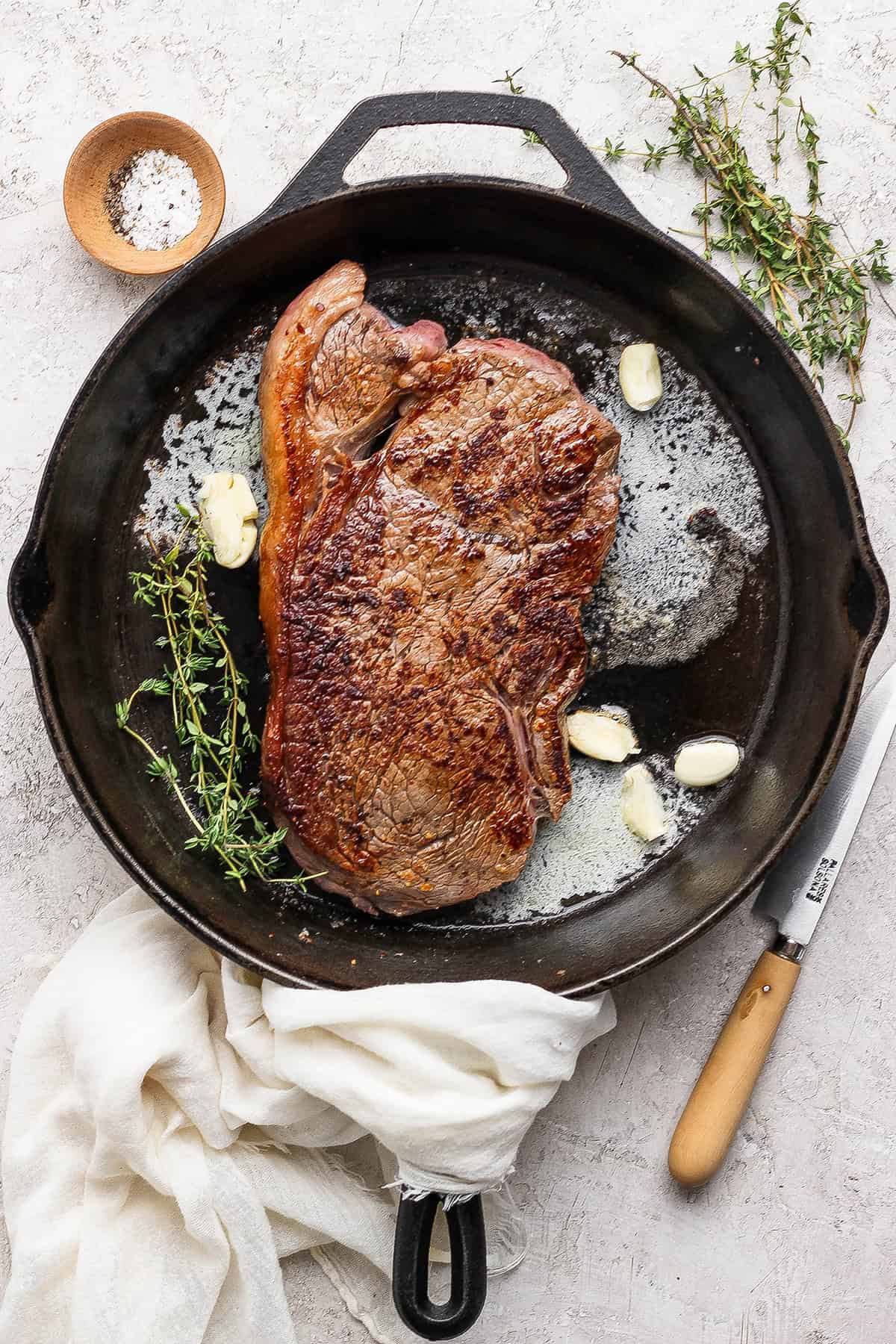 Steak in cast iron skillet with thyme, garlic cloves, and butter.