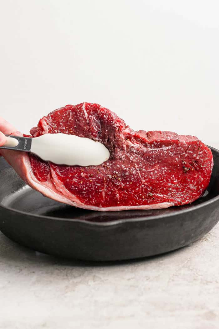 Tongs placing steak into cast iron skillet.