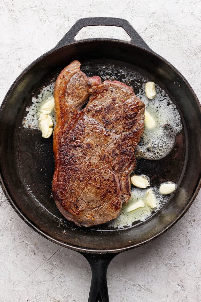 Steak in cast iron skillet with smashed garlic and butter.