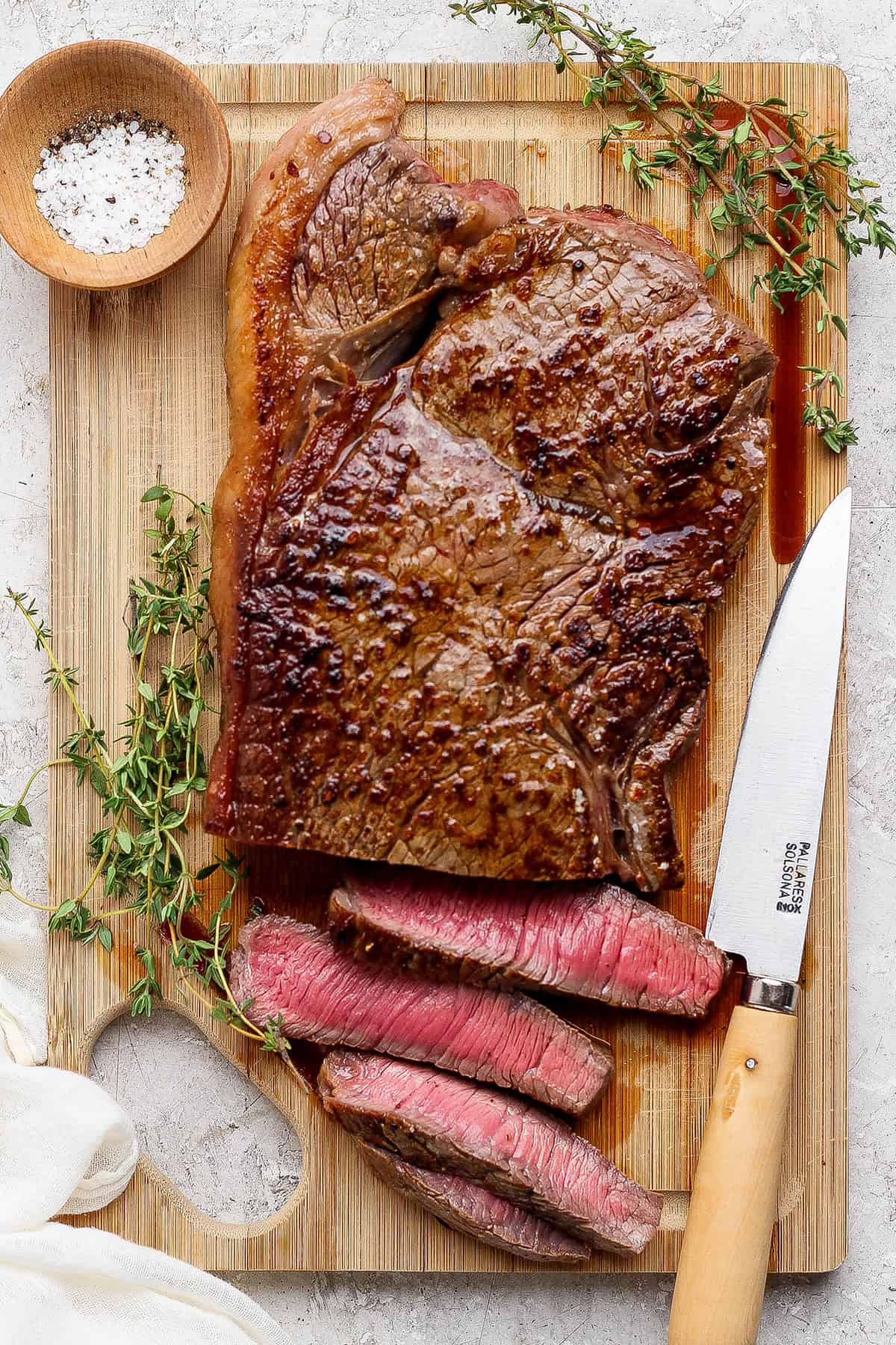 Cast iron skillet steak on board with 4 slices cut.