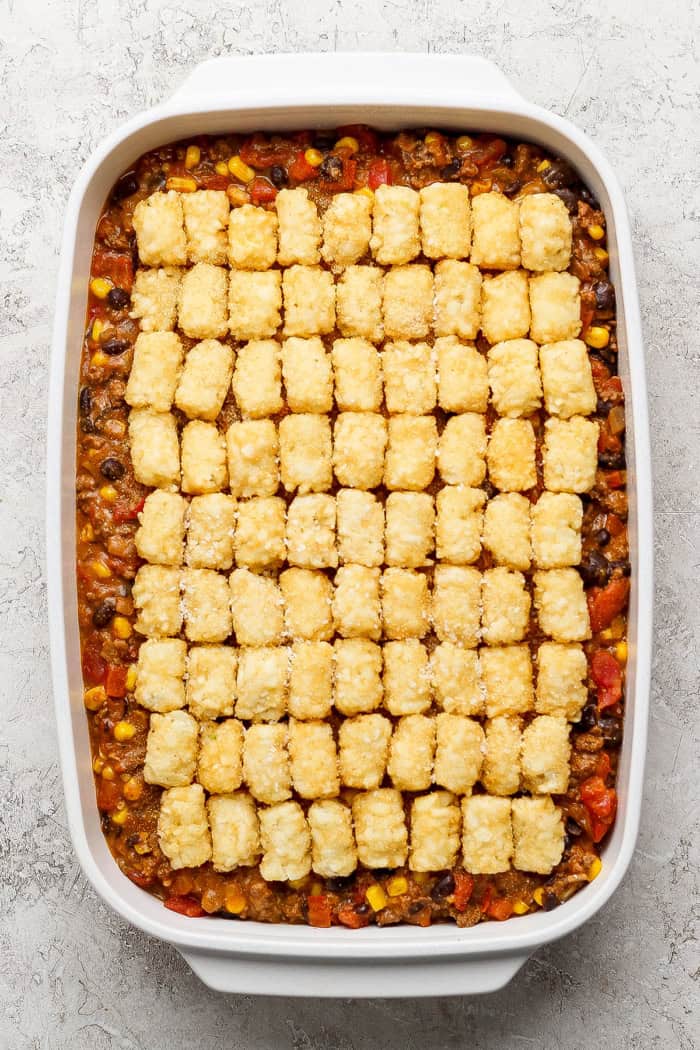 overhead photo of taco casserole topped with frozen tater tots, in a white 9 x 13 baking pan
