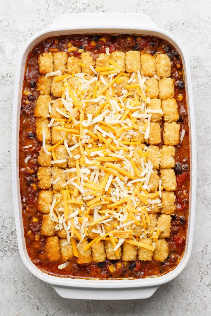 overhead photo of taco casserole topped with frozen tater tots and cheese, in a white 9 x 13 baking pan