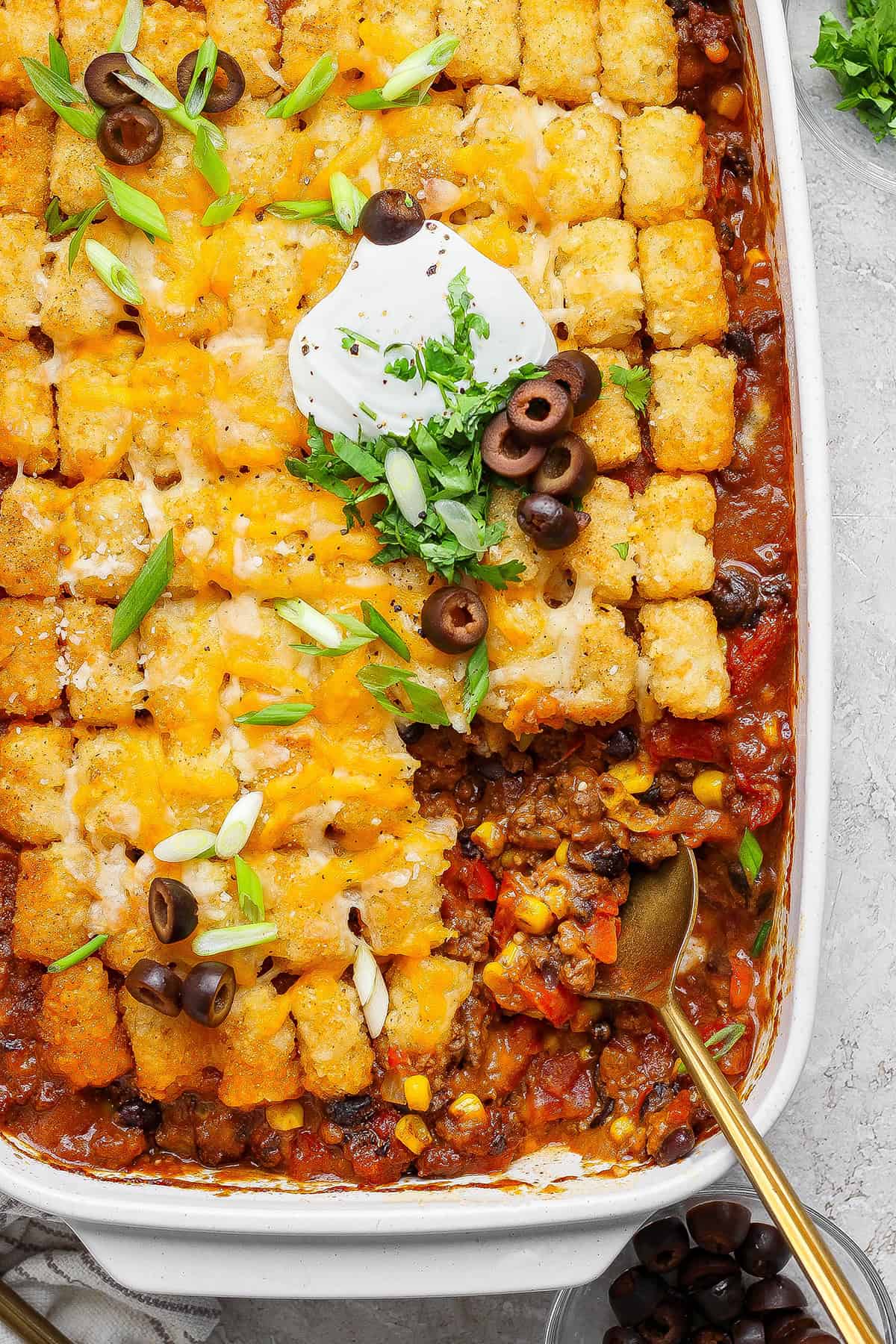 overhead photo of taco tater tot casserole in a white 9 x 13 baking pan, with a portion removed