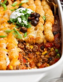 taco tater tot casserole in a white baking dish, with a portion removed