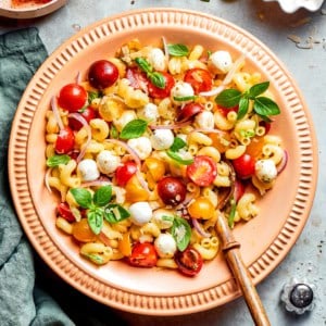 overhead photo of pasta caprese salad in a peach-colored serving bowl