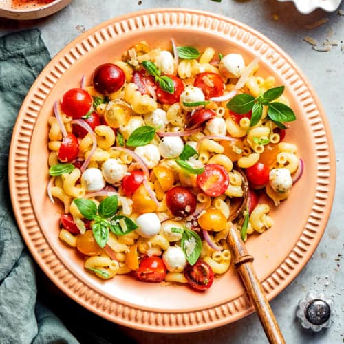 overhead photo of pasta caprese salad in a peach-colored serving bowl