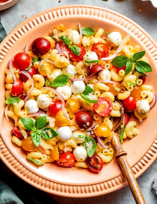 overhead photo of pasta caprese salad in a peach-colored serving bowl