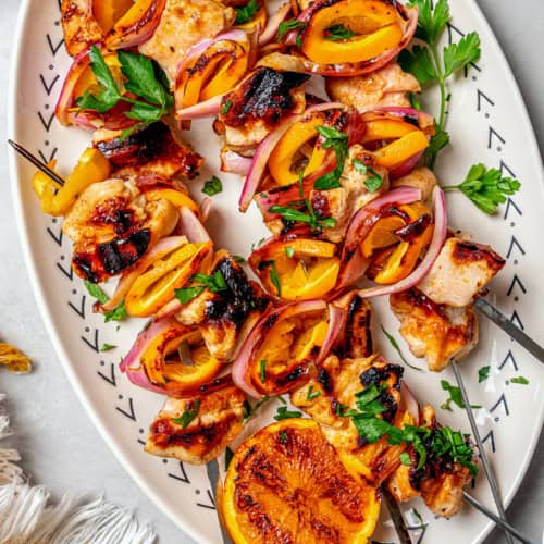 overhead photo of grilled turkey kabobs with orange slices on a white oval platter