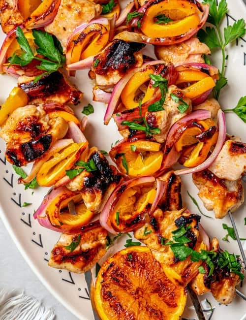 overhead photo of grilled turkey kabobs with orange slices on a white oval platter
