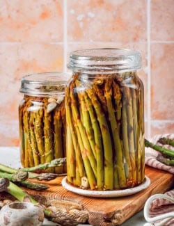 two jars of pickled asparagus on a wood cutting board