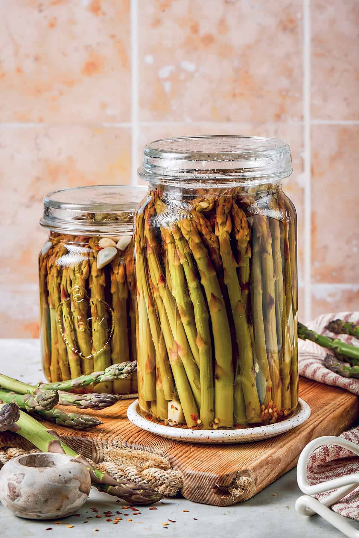 two jars of pickled asparagus on a wood cutting board