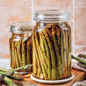 two jars of pickled asparagus on a wood cutting board