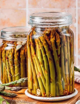 two jars of pickled asparagus on a wood cutting board