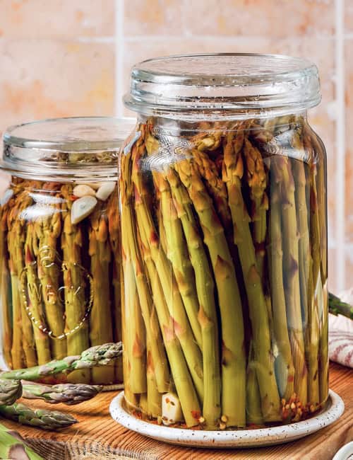 two jars of pickled asparagus on a wood cutting board