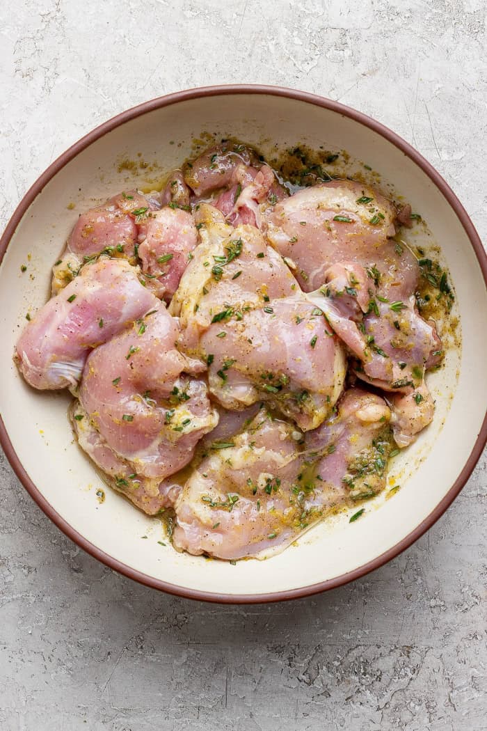 Chicken thighs in bowl with lemon herb marinade.